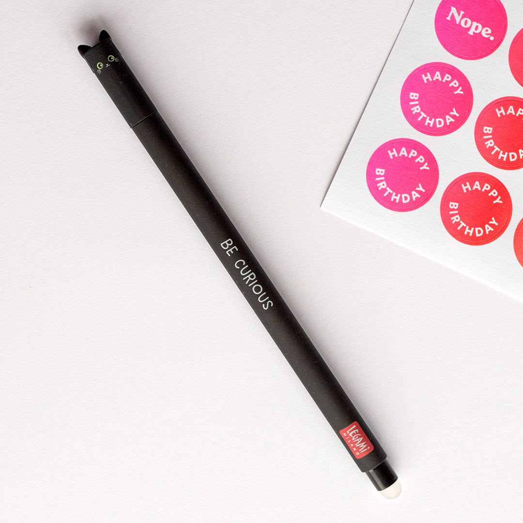 Black Legami pen with a cat-shaped top on a white surface next to pink 'Happy Birthday' stickers.