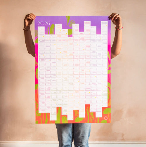 Person holding a large colorful A1 2026 calendar poster for gardening with 2026 on a plain wall.
