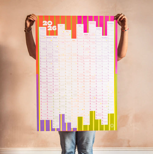 Person holding a colorful 2026 calendar against a plain wall