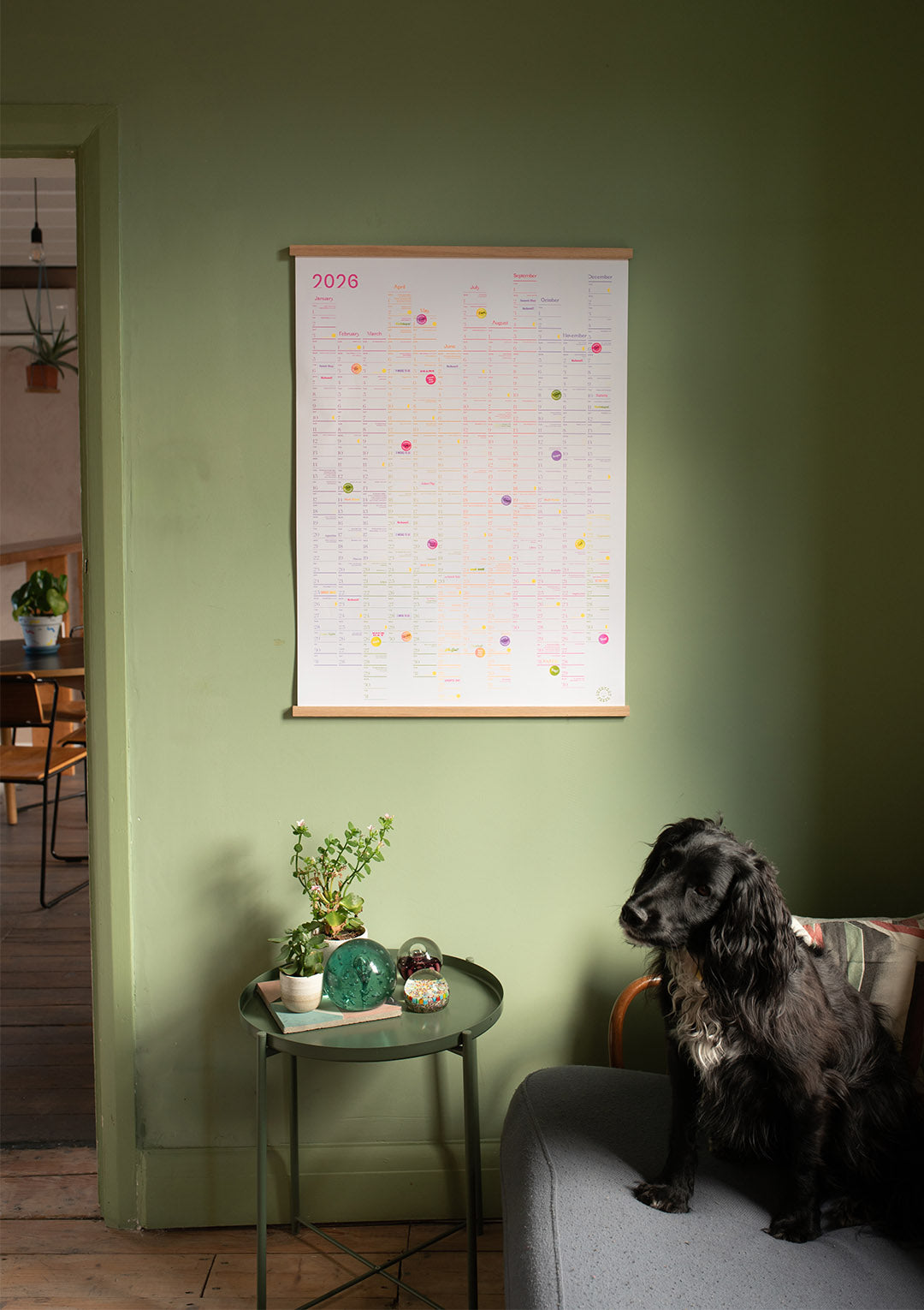 Dog sitting on a couch next to a green side table with a plant, against a green wall with a calendar. Luckyday Press Classic all Planner Ladyland press