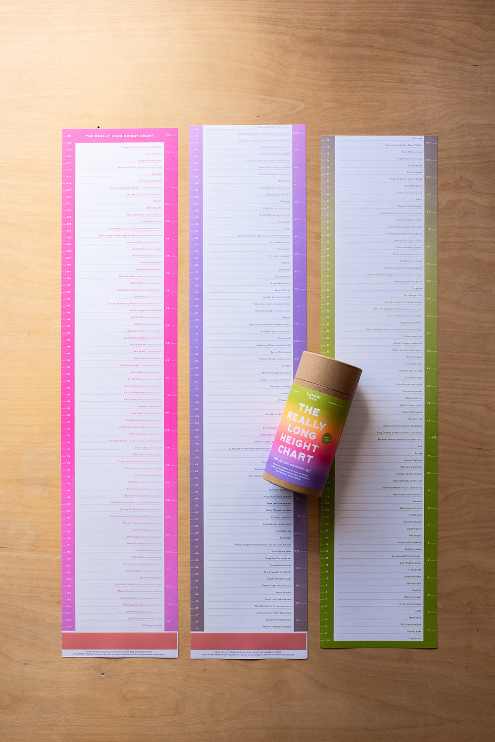 Three colorful sections of height charts on a wooden surface with a cylindrical object on top. Luckyday Press Really Long Height Chart Ladyland press