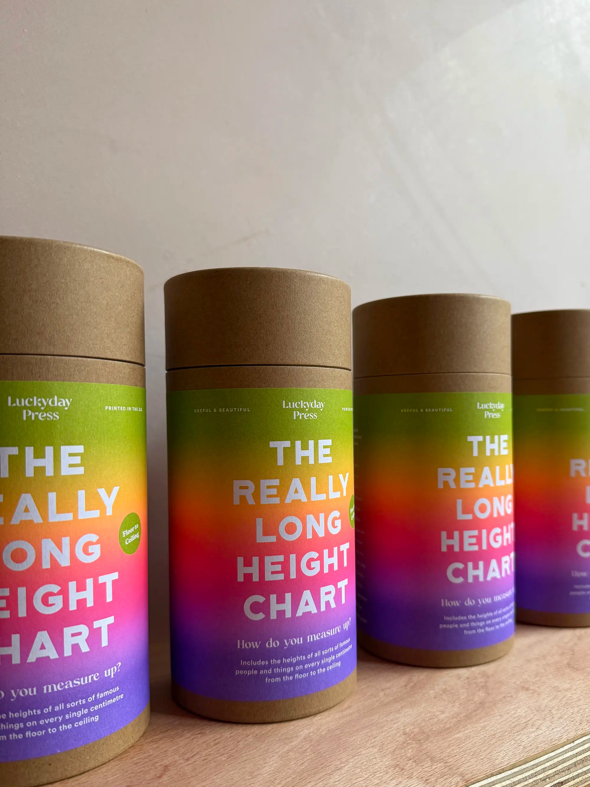 Four cylindrical height charts with gradient designs on a wooden surface. Luckyday Press Really Long Height Chart Ladyland press